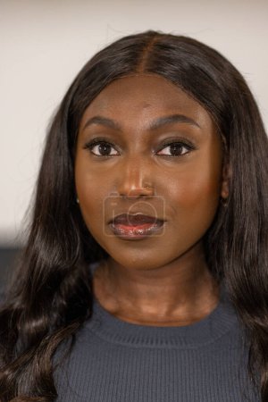 This image captures a close-up portrait of an African American woman with a confident gaze. Her dark eyes are highlighted with subtle makeup, and her lips are adorned with a glossy finish. Her skin