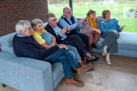 Aufgenommen in einem zeitgenössischen Wohnraum, zeigt dieses Foto eine Gruppe von Senioren, die sich intensiv mit ihren Smartphones beschäftigen. Sie sitzen zusammen auf einer bequemen Couch, was auf eine Verschmelzung von moderner