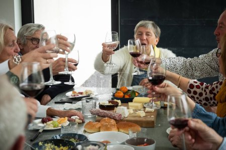 In this vibrant scene, senior friends share a toast over a table laden with a gourmet selection of cheeses, bread, and fruits. Laughter and cheer are evident as glasses are raised in celebration. The