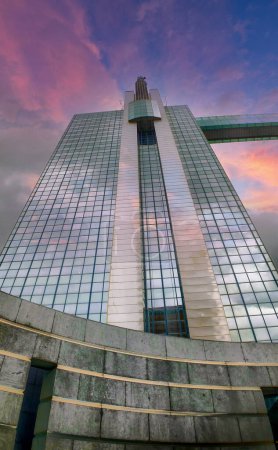 The grandeur of an Art Deco skyscraper is magnified against the canvas of a dramatic sunset sky. The buildings reflective glass captures the fading light, while architectural details stand