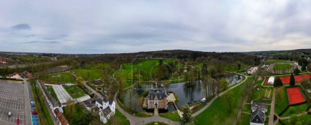 Photo for Huizingen, Belgium, 26th of March, 2024, This panoramic aerial image beautifully captures the lush, verdant landscape of Huizingen, featuring a historic castle by a serene lake. The sprawling greens - Royalty Free Image