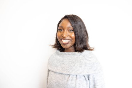 This portrait captures a joyful young Black woman wearing a cozy gray turtleneck sweater. Her radiant smile and sparkling eyes convey a sense of happiness and warmth. The clean white background