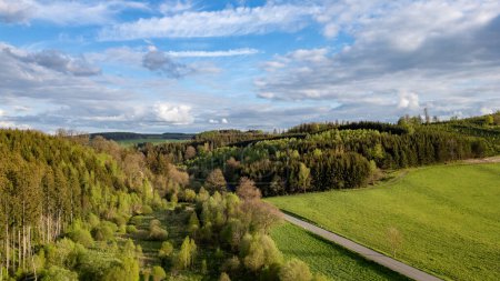 This striking aerial photograph showcases the diverse landscape of the Hautes Fagnes region, featuring a mix of dense forest areas and vibrant green fields. The image captures the natural beauty of