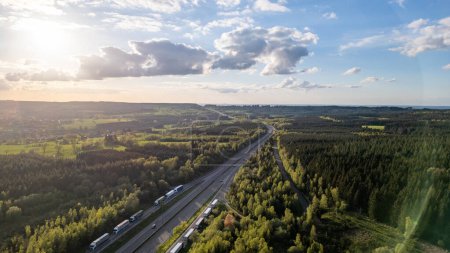 Dieses Luftbild zeigt die Autobahn E42, die sich bei Sonnenuntergang durch die grünen Wälder der Region Hautes Fagnes schlängelt. Die Straße wird von dichten Wäldern flankiert, die eine atemberaubende Landschaft präsentieren