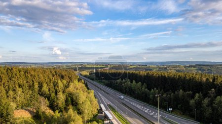 Dieses Bild bietet einen erhöhten Blick auf die Autobahn E42, die sich durch die dicht bewaldete Region Hautes Fagnes bei Emmels schlängelt. Das üppige Grün, das die Straße umhüllt, steht in schönem Kontrast zu