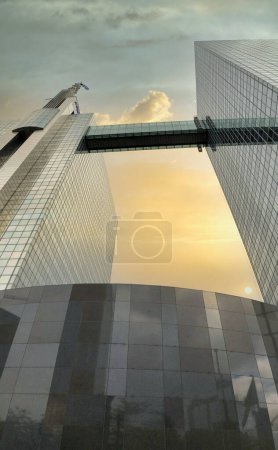 A stunning urban sunset, with its soft gradients from orange to blue, reflects on the sleek glass facade of a modern skyscraper. The suns descent casts a golden glow over the building, creating a