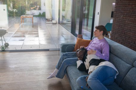 Esta imagen cuenta con dos mujeres que se relajan en un sofá en una sala de estar contemporánea, mostrando un momento cómodo y sereno. Una mujer, que parece ser blanca, está sentada erguida mientras que la otra mujer