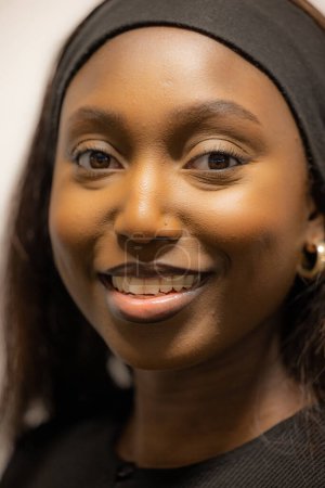 This image features a close-up portrait of a smiling Black woman wearing a black headband. Her dark, expressive eyes and radiant smile are the focal points of the image, highlighting her natural