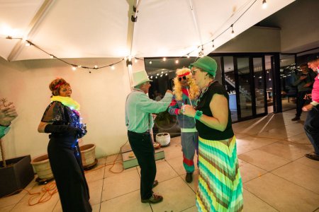 A group of friends is having a great time at a retro costume party, dancing on a rooftop under sparkling string lights