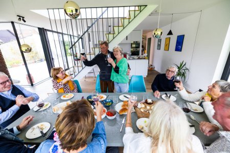 Un grupo de personas mayores reuniéndose, disfrutando de una comida y vino en un moderno comedor lleno de risas y vítores