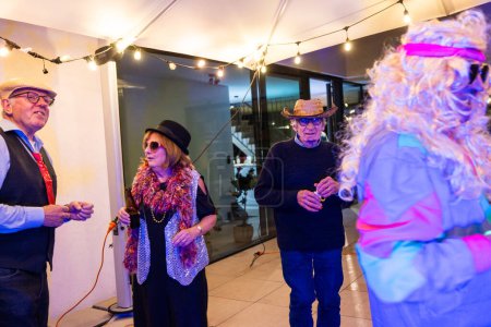 Ältere Freunde in festlichen Kostümen und Hüten vergnügen sich bei einer Party, trinken und tanzen zusammen