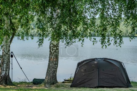 A serene camping setup by the lake with a tent and trees, creating a peaceful atmosphere blending nature and relaxation