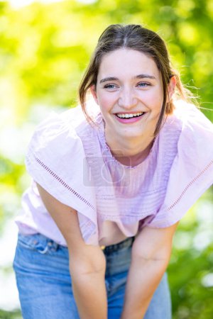 This image features a young woman bending forward in laughter, with sunlight filtering through the leaves to illuminate her face. Her joy is infectious, highlighted by the bright summer day. Shes