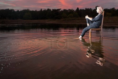 A person peacefully enjoys a beautiful sunset while sitting on a chair partially submerged in calm water