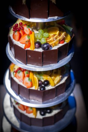 Magnífico pastel de varios niveles adornado con deliciosas frutas y rico chocolate, un postre espectacular y deliciosa