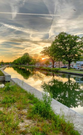Stadtkanal, baumbewachsen, reflektiert atemberaubenden Sonnenuntergangshimmel mit Kondensstreifen und schafft friedliche Außenlandschaft
