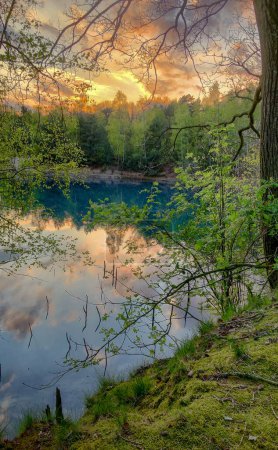 Ein ruhiger Waldsee, umgeben von lebendigem Grün, spiegelt einen atemberaubenden Sonnenuntergang Himmel schafft eine atemberaubende Landschaft