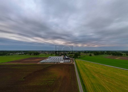 An aerial view of farmland fields and buildings under a dramatic cloudy sky, capturing the beauty of the landscape