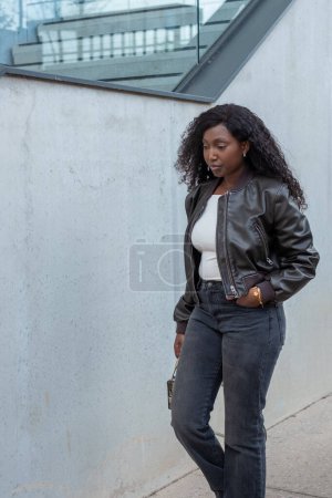 A fashionable young woman is walking outdoors in a leather jacket and jeans, showcasing city street style