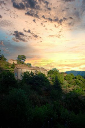 A tranquil sunrise illuminates a rustic house in the green mountains, showcasing the serene beauty of the countryside