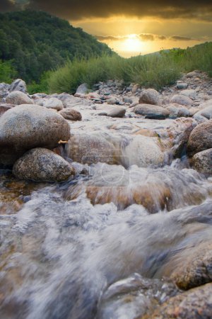 A serene creek flows through rocky terrain with a stunning sunset, creating a picturesque natural landscape