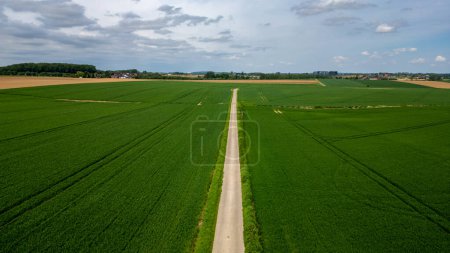 An aerial view of a road cutting through green fields under a cloudy sky, showing a serene rural landscape