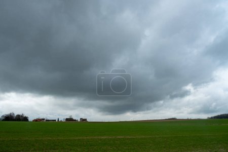 Nubes de tormenta oscura baja cuelgan sobre el exuberante campo verde, enmarcando los edificios agrícolas distantes en el horizonte