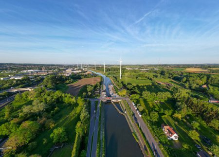 Foto de Sluis van Lot, kanaal Brussel, Charleroi, Lot, Beersel, 18 de mayo de 2024 Esta amplia imagen aérea ofrece una vista panorámica de un pintoresco canal cubierto de turbinas eólicas y rodeado de campos verdes. - Imagen libre de derechos