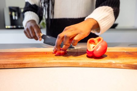 Closeup view of hands delicately slicing a vibrant red bell pepper on a wooden cutting board in a contemporary kitchen