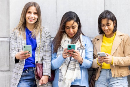 Three young women using smartphones outdoors, representing modern lifestyle with technology and connectivity