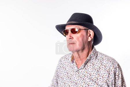Stylish elderly man in patterned shirt, sunglasses, and hat poses for portrait, exuding trendy and cool vibe
