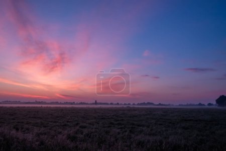 Le lever du soleil est magnifique sur un champ brumeux, mettant en valeur des couleurs vives dans le ciel et un horizon brumeux