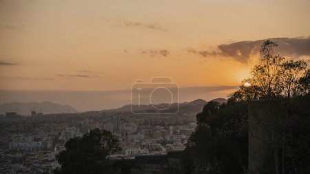 Photo for Distant view of historical Cathedral of Malaga amidst cityscape and silhouette mountains against sky during sunset at Malaga, Andalusia, Spain - Royalty Free Image