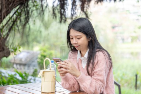 Photo for Taiwanese woman in her 20s sitting in a park in Matsuyama Wenso Park, Xinyi District, Taipei City, Taiwan, operating her smartphone - Royalty Free Image