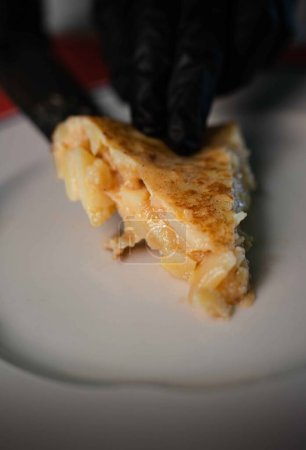 Savor the moment as you behold a freshly cut portion of classic Spanish tortilla, delicately placed on a pristine plate. The golden hue of the tortilla contrasts beautifully with the clean white backdrop, enticing you with its irresistible aroma and 