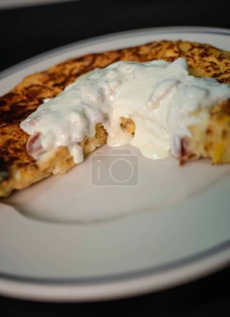 Experience a delightful blend of Spanish tradition and Italian flair with our savory potato omelet, featuring tender potatoes, eggs, and a luscious carbonara sauce. Served on a pristine white plate against a striking black backdrop, it's the perfect 