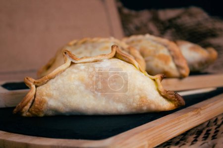 Genießen Sie die authentischen Aromen Argentiniens mit unseren leckeren Empanadas, die elegant auf rustikalen Holzbrettern vor warmem Papphintergrund präsentiert werden. Jeder Bissen ist eine Reise durch das pulsierende kulinarische Erbe Argentiniens, perfekt zum Hinzufügen