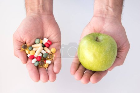 Téléchargez les photos : Main de l'homme avec un avec une pomme verte et main avec des pilules - en image libre de droit