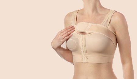 Young woman wearing a compressing bra with a stripe after breast augmentation surgery. 