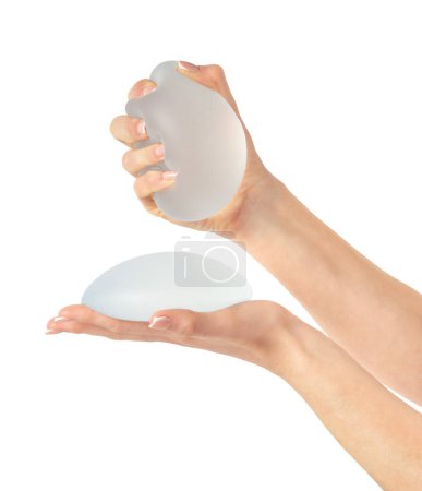 Téléchargez les photos : Main féminine serrant l'implant mammaire rond doux sur fond blanc. Mammoplastie - en image libre de droit