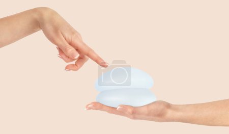 Téléchargez les photos : Main féminine pointant sur les implants mammaires sur fond beige, mammoplastie. - en image libre de droit