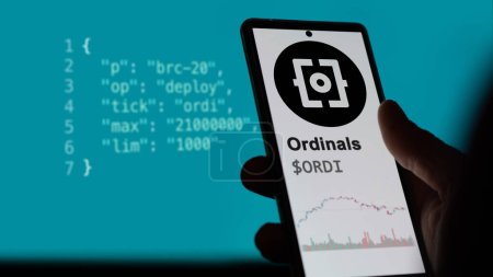 Photo for May 12th 2023. An investor analyzing the price of Ordinals token on a phone, $ORDI asset trend on a screen in the foreground. BRC-20 concept script on the background. - Royalty Free Image