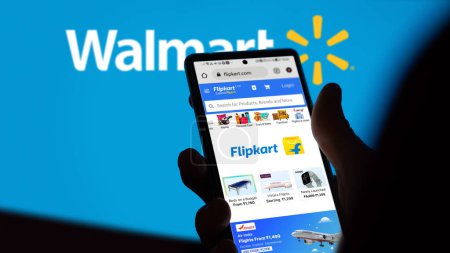 Foto de 31 de julio, alguien sostiene un teléfono en el sitio de Flipkart, en el fondo una parte del logotipo borroso de Wallmart. - Imagen libre de derechos
