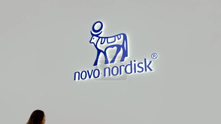 Photo for Focus on the logo of Novo Nordisk in a business district, on the foreground a blurry passer-by. - Royalty Free Image
