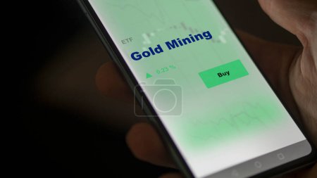 Photo for An investor analyzing the gold mining etf fund on a screen. A phone shows the prices of Gold Mining - Royalty Free Image