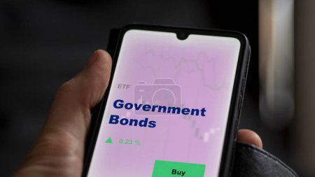 Photo for An investor analyzing the government bonds etf fund on a screen. A phone shows the prices of Government Bonds - Royalty Free Image