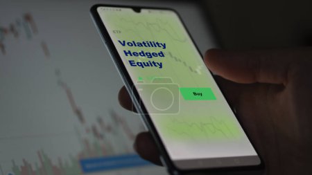 Photo for An investor analyzing the volatility hedged equity etf fund on a screen. A phone shows the prices of Volatility Hedged Equity - Royalty Free Image