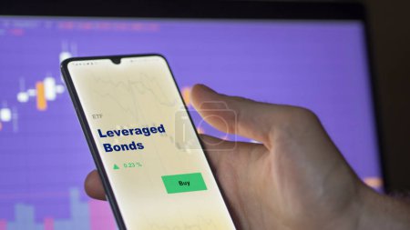 Photo for An investor analyzing the leveraged bonds etf fund on a screen. A phone shows the prices of Leveraged Bonds - Royalty Free Image