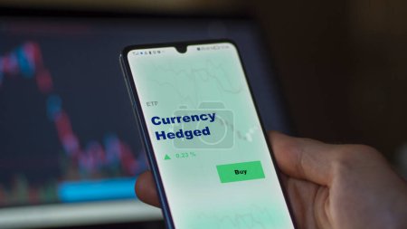 Photo for An investor analyzing the currency hedged etf fund on a screen. A phone shows the prices of Currency Hedged - Royalty Free Image