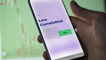 Photo for An investor analyzing the low correlation etf fund on a screen. A phone shows the prices of Low Correlation - Royalty Free Image